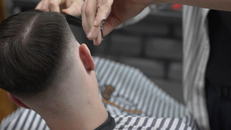 Professional barber cutting clients hair with scissors and comb, creating a stylish fade in a modern barbershop, providing a high quality grooming serviceの写真素材