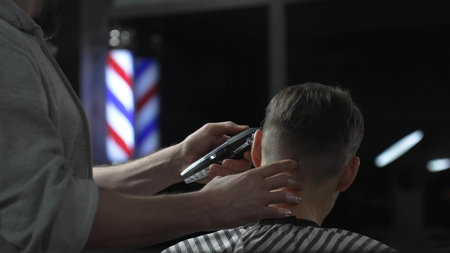 Skilled barber trimming clients hair with electric razor, creating precise contemporary hairstyle...