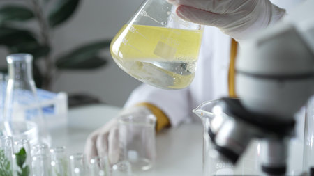 A scientist wearing white protective gloves is shaking up a yellow chemical solution inside an...