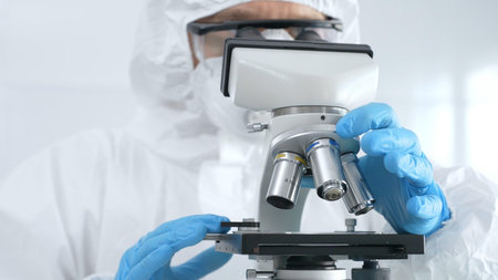 Medical virologist in a hazmat suit, mask, and blue protective gloves, carefully working at a...