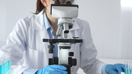Female scientist wearing protective gear carefully adjusting microscope lens, analyzing medical...