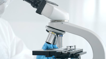 Close up of medical virologist in a hazmat suit, mask, blue gloves, working at a microscope in a...