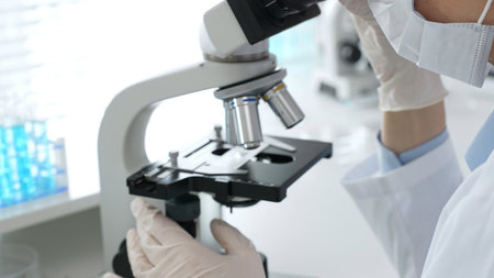 White gloved hands of scientist professional adjusting a microscope in a bright laboratory,...