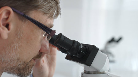 Close up of a male scientist looking through a microscope, conducting research and analysis in a...