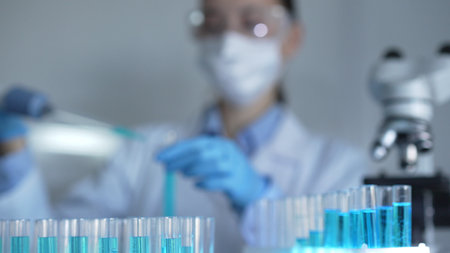 Laboratory tubes are in focus, closeup view. Female scientist researcher is using a micropipette at...