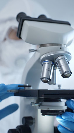 Medical virologist in a hazmat suit, mask, and gloves, diligently working at a microscope in a...