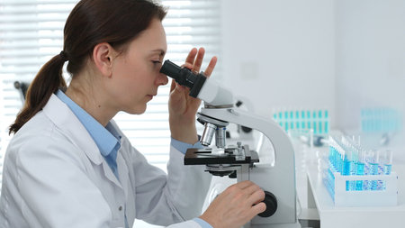Female scientist examining microscope slide, analyzing chemical sample in sterile laboratory...