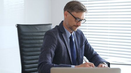 Adult businessman wearing blue suit, tail and glasses is concentrating while writing on a document...
