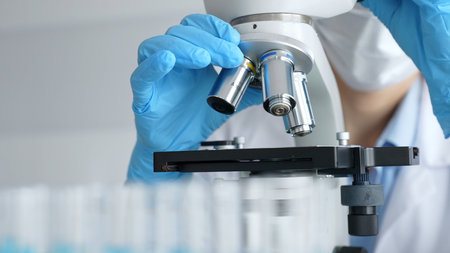 Close up of scientists gloved hands adjusting microscope, conducting research in laboratory with...