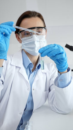Close up of scientist wearing mask and gloves adding fluid to test tube using pipette in laboratory...