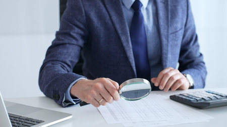 Professional accountant is examining financial documents, magnifying glass in hand, calculator...