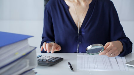 Professional female accountant analyzing financial documents, using magnifying glass and calculator...
