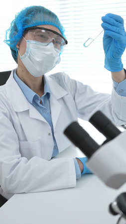 Medical science researcher wearing blue protective gear of cap, gloves and googles, is examining...