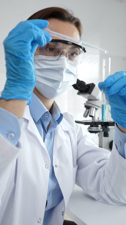 Close up of scientist wearing mask and gloves adding fluid to test tube using pipette in laboratory...