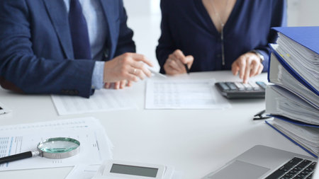 Magnifying glass and calculator over financial documents opposite financial team of male and female...