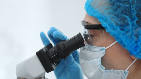 Scientist examining sample under microscope, wearing protective lab gear, performing detailed...