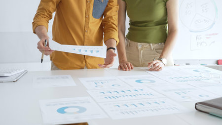 Professional team analyzing financial charts, collaborating intently around conference table in...