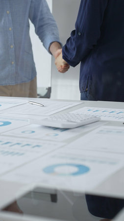 Business partners shaking hands after successful agreement over financial documents, calculator and...