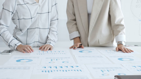 Two businesswomen examining financial data on charts and graphs during an office meeting,...