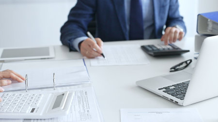 Two accountants are collaborating on a project, using a calculator and taking notes, surrounded by...