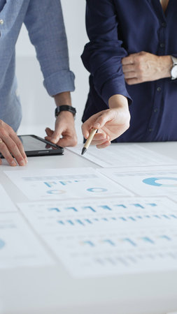Professional team reviewing financial documents, pointing at charts on desk, collaborating to...