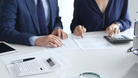 Calculator and magnifying glass over financial documents opposite financial team analyzing data,...