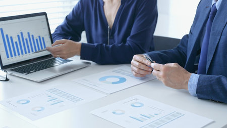 Businessman and businesswoman are analyzing financial data on a laptop and printed documents,...