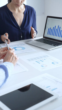Businessman and businesswoman using laptop while looking through documents, pointing at charts and...