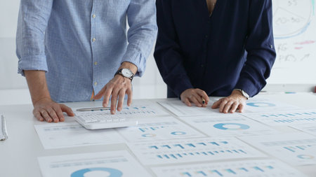 Focused business professionals analyzing financial charts and graphs, discussing market trends and...