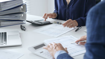 Business team of male and female accountants analyzing financial documents, using calculators and...