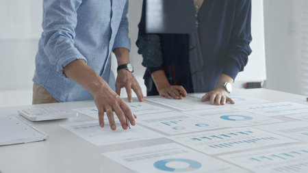 Business professionals analyzing financial charts, gesturing over spreadsheets during collaborative...