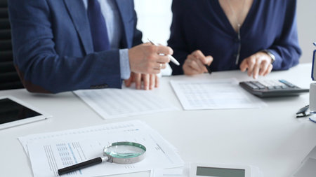 Close up of magnifying glass and calculator over financial documents opposite financial team,...