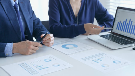 Businesspeople reviewing financial documents, collaborating over laptop screen, analyzing market...