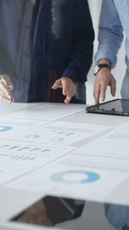 Professional team reviewing financial documents, pointing at charts on desk, collaborating to...