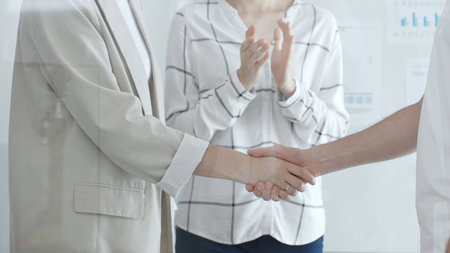 Professional businesswomen greeting, handshaking after closing deal, male coworker clapping in contemporary office setting. Business people conceptの写真素材