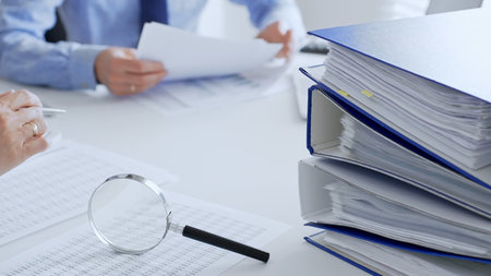 Accountants are analyzing financial reports with magnifying glass and documents, performing...