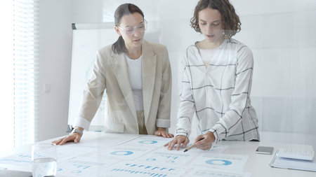 Professional businesswomen analyzing financial charts, collaborating in sleek corporate workspace, highlighting data. Business people conceptの写真素材