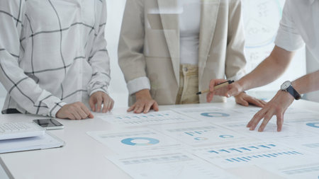 Professional team reviewing financial data, working together on charts and graphs in bright office,...