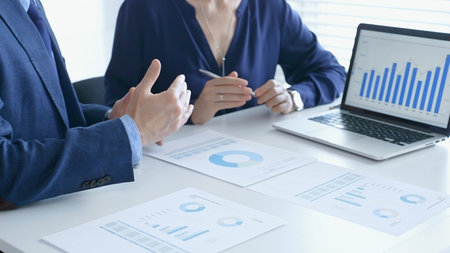 Businessman and business woman reviewing financial documents, collaborating over laptop screen,...