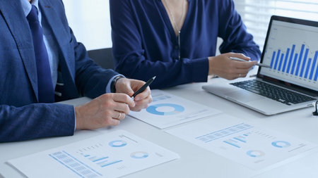 Business team analyzing financial data on a laptop and printed documents, pointing at charts and...