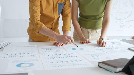 Business professionals analyzing financial reports, pointing at charts during collaborative meeting,...