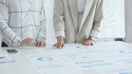 Professional women analyzing financial charts, discussing business strategy in modern light office,...