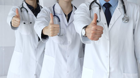 Doctor team showing thumbs up, symbolizing healthcare success, medical approval, achieving goals, quality patient care, positive health outcomes, and professional supportの写真素材
