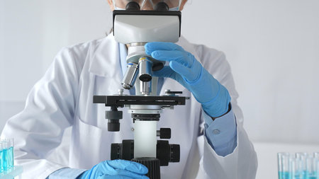 A female scientist in protective gear adjusts a microscope lens and accurately analyzes medical...
