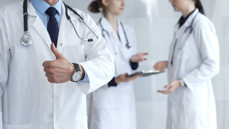 Doctor giving thumbs up sign for medical approval while standing with health practitioners,...