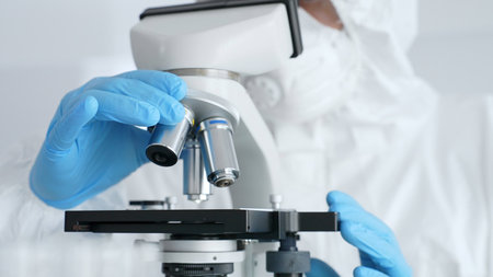 Close up of scientific researcher or virologist wearing protective gear is adjusting microscope, analyzing lab samples with precision in sterile research environment. Medicine and science conceptの写真素材