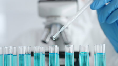 Close up of scientific researcher wearing protective gear, carefully pipetting liquid into test tubes while conducting medical research experiment in laboratory. Medicine, healthcare and science conceptの写真素材