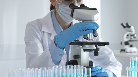 Scientist wearing protective gear carefully adjusting microscope lens, analyzing medical research...