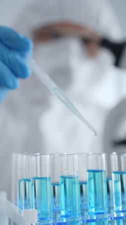 Close up of scientific researcher or virologist wearing protective gear, carefully pipetting liquid...