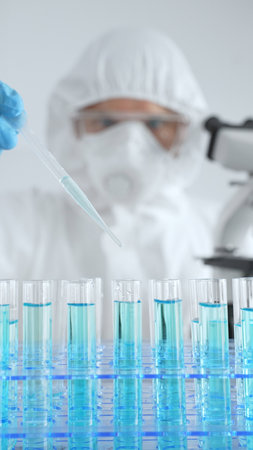 Scientific researcher wearing protective gear, carefully pipetting liquid into test tubes while conducting medical research experiment in laboratory. Medicine, healthcare and science conceptの写真素材